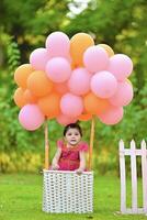 A baby sitting in a basket with balloons photo