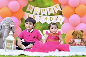 Two children in pink dresses sitting on a blanket with balloons photo