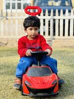 A young boy riding a toy car in the yard photo