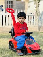 A young boy sitting in a red toy car photo