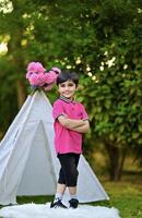 A young boy in pink shirt standing in front of a teepee photo
