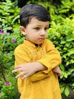 A young boy in yellow standing in front of some bushes photo