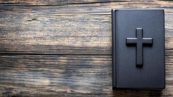 A cross resting on a black book placed on a rustic wooden background with space photo