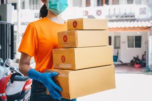 Delivery service courier holding boxes mail for sending to customer while wearing mask and glove for protect herself in covid-19 pandemic outbreak. photo