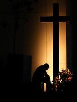 A priest in deep prayer before a cross illuminated at night in a peaceful location photo