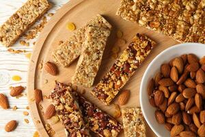 Board with granola bars and bowl with almond on wooden background, top view photo