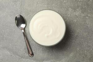 Spoon and bowl of sour cream on gray background, top view photo