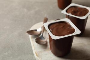 Board with plastic cups of yogurt and spoons on gray background photo