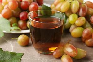 Glass of juice and plate with grape on gray background photo