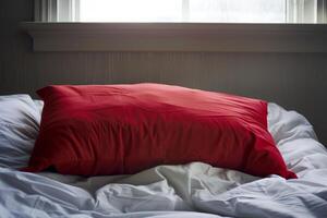 Single red pillow laying on an unmade bed with a window behind photo