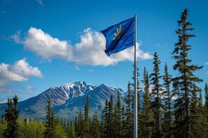 Alaskan flag waving in the wind with snow capped mountains and forest photo