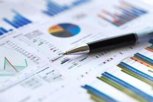 Ballpoint pen lying on documents with financial statistics charts and graphs background photo