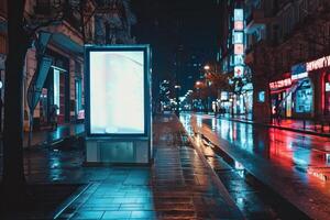 Blank billboard illuminating empty city street at night reflecting on wet pavement photo