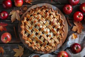Delicious apple pie is surrounded by red apples and autumn leaves on a rustic wooden table photo