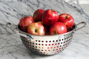 Red apples sitting in a metal colander on a marble countertop photo