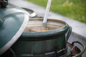 Large green metal pot with open lid and ladle serving soup outdoors on a rustic cooking setup photo