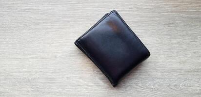 Black or brown leather wallet on light brown wooden table or background with copy space. Object, Money and Shape concept. photo