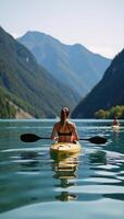 Woman paddling a kayak along serene river nestled amidst green mountains Back View photo
