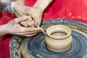 Two pairs of hands mold something from clay on a potter's wheel photo