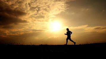 Silhouette of a Person Running at Sunset with Dramatic Clouds and Golden Sky in the Background photo