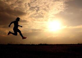 Silhouette of a Person Running at Sunset with Dramatic Sky and Clouds in the Background photo