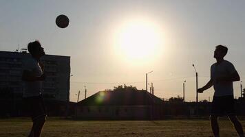Silhouette of professional footballers kicking soccer ball with their heads on stadium at sunset. Two sportsmen showing tricks with ball while passing it to each other at field. Freestyle football photo