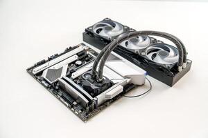 An isolated view of a stylish white themed gaming motherboard equipped with a CPU liquid cooling system. It features a sleek black and white color scheme with vivid RGB lighting accents. photo