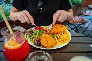 A crispy schnitzel garnished with fresh herbs, served with a vibrant side salad of mixed greens, tomatoes, and cucumber, along with golden french fries and a refreshing glass of red juice. photo