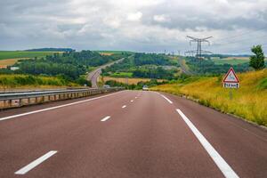 France, The road stretches ahead, flanked by lush green fields under a partly cloudy sky. The scene captures the essence of a peaceful drive, inviting adventure and exploration in the open countryside. photo