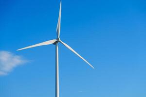 A large white wind turbine with three blades towers against a clear blue sky, symbolizing clean energy. It harnesses wind power for sustainable electricity generation, contributing to a greener future. photo