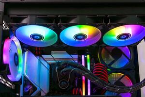The image depicts an open black computer case featuring several cooling fans glowing in bright rainbow colors. The case has a tempered glass side panel, showcasing the fans arranged vertically. photo