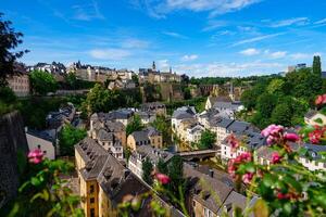 Luxembourg . The image showcases a beautiful cityscape of an ancient European city, with a serene river flowing through. Lush green hills frame the scene, emphasizing a charming mix of historic and modern architecture. photo