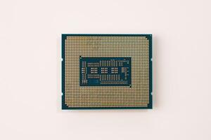 The image shows a closeup of the backside of a computer processor chip, highlighting intricate gold pins and contact points against a white background, emphasizing the complexity of modern technology. photo