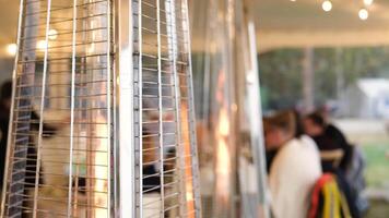 Slow motion captures a gas patio heater burning, creating a warm ambiance for diners in the background video
