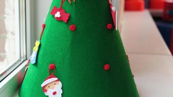 Woman decorates a green felt christmas tree with colorful felt ornaments, creating a festive atmosphere in slow motion video