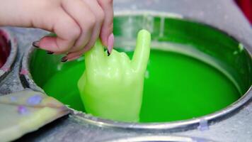 Woman repeatedly dips a hand-shaped mold into a vat of green wax, creating a layered effect in slow motion video