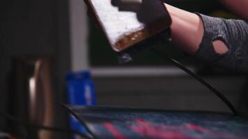 Female hands of a craftsman in a ski equipment repair shop. Applying wax with an iron to the sliding surface of a snowboard. Close-up. Shallow depth of field video