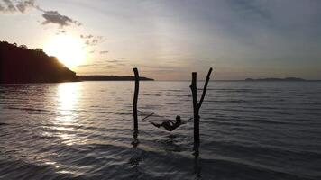 Woman lying in a hammock in the sea silhouette background is an island and the sea in the evening.Evening activities on a holiday to the sea video