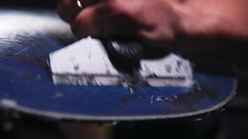 Snowboard sliding surface repair process. Close-up with shallow depth of field. The technician scrapes off excess wax applied to the snowboard. video