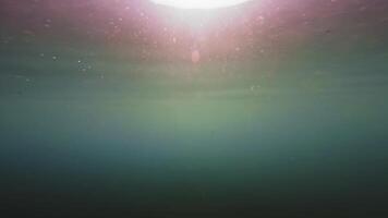 View of sun light from blue abyss, slow motion. Light filters down through blue water. Underwater sun rays in depth ocean. Underwater sun light shine under deep water with ripples on waves surface video
