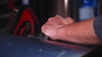 Female hands of a snowboard repairman cleaning wax off the sliding surface of a snowboard. Close-up with shallow depth of field. Low key video