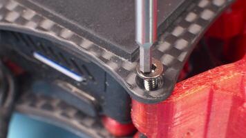 Macro close-up. Screwdriver unscrews a remote hex screw in the carbon fiber frame of a self-assembled quadcopter. The top plate and power wires are in the frame. selective focus video