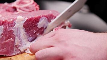 close-up hands of a man cutting raw pork meat with a knife on a board on the kitchen table video