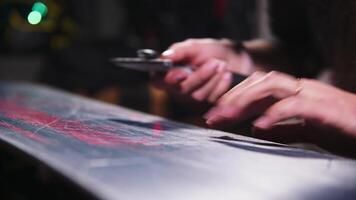 Female hands of a snowboard repairman cleaning wax off the sliding surface of a snowboard. Close-up with shallow depth of field. Low key video