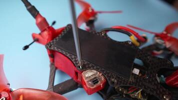 Close-up of diy drone on blue desktop. Disassembling and repairing drone at home. Hex screwdriver unscrews carbon frame of self-assembled fpv quadcopter video