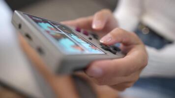 Close-up in shallow depth of field. Unrecognizable portable retro console in hands of young Caucasian woman. Girl plays retro games holding retro device for emulating old console games video