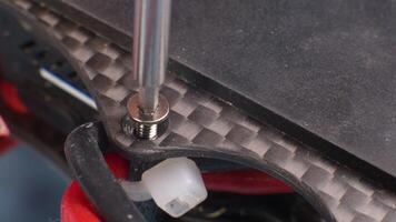 Macro close-up. Screwdriver unscrews a remote hex screw in the carbon fiber frame of a self-assembled quadcopter. The top plate and power wires are in the frame. selective focus video