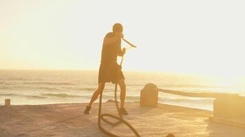 Determined sporty man practicing air boxing with battle rope at sunset video