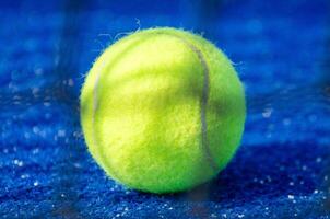 A ball on a paddle court, with the net out of focus in the foreground. photo