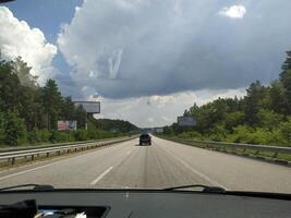 A tranquil drive along a highway surrounded by lush greenery and majestic clouds under the open sky on a warm afternoon photo